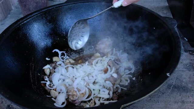 Female hand stirs pilaf which steam rises. Cooking pilaf in cauldron, lamb meat with tail fat. Mouth-watering video where traditional pilaf dish is cooked. Chef uses the lamb meat that's cooked with t