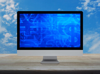 Financial currency symbol on desktop computer monitor screen on wooden table over blue sky with white clouds
