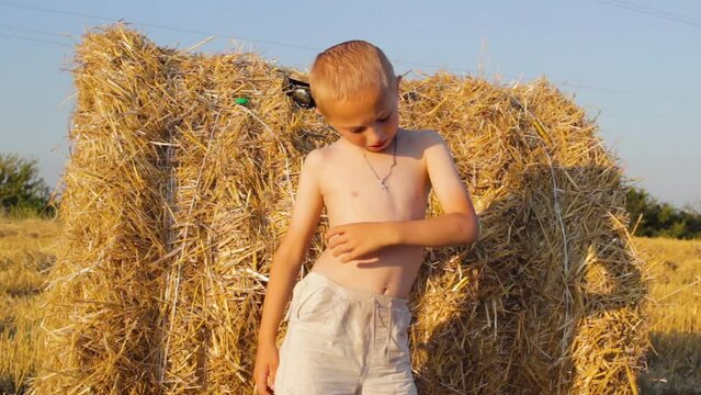 a boy near a haystack at sunset,in the summer, the boy stands wet in the field