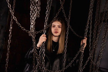 Stylish classy teen girl model 12-13 year posing in dark industrial room with chains, looking at camera. Cute chic teenage girl actress in leather jacket. Fashionable image concept. Copy ad text space