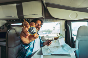 Travel and adventure people lifestyle. One man portrait showing compass and using road map paper to choose next trip destination. People and vehicle camper van interior. Vanlife offgrid. Home vacation