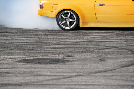 side view of yellow sport car drifting on gray speed tarmac track with smoke coming out of the back  tire wheel