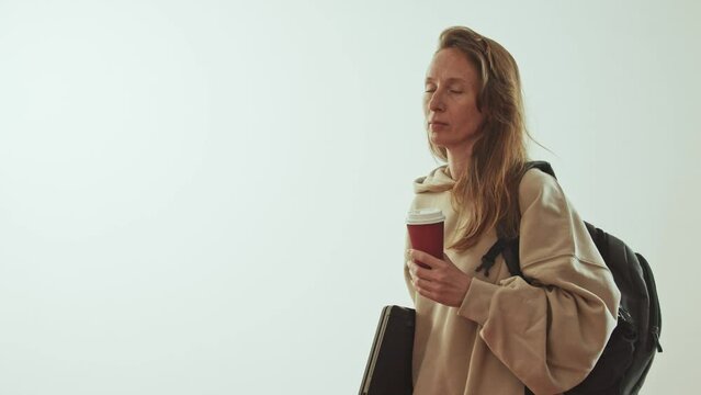 Young adult woman with a backpack, a laptop and a paper glass of coffee on a white background. Foreign student. Volunteering in UN programs