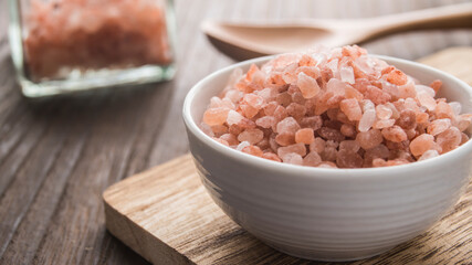 Himalayan pink salt in a white dish in the foreground on a wooden table.
