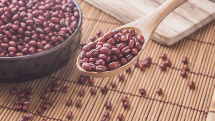Beans typical of Japan in a plate on a table. Wooden spoon and some grains scattered on the table. Red beans . Azuki. 