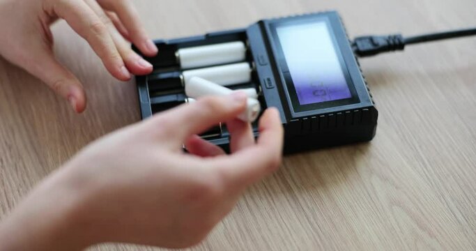 Female hands insert cells for battery into charger. AA battery charger