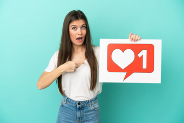 Young caucasian woman isolated on blue background holding a placard with Like icon and pointing it