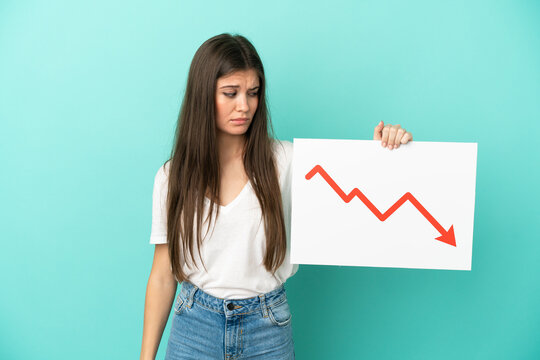 Young caucasian woman isolated on blue background holding a sign with a decreasing statistics arrow symbol with sad expression