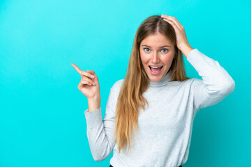 Young blonde woman isolated on blue background surprised and pointing finger to the side