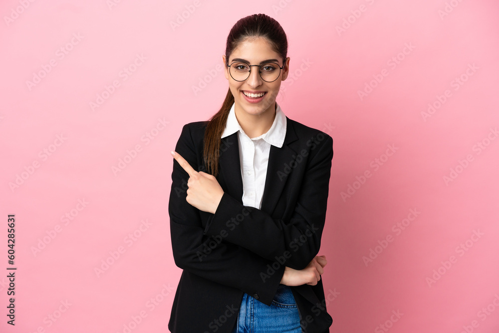 Wall mural Young caucasian business woman isolated on pink background pointing to the side to present a product