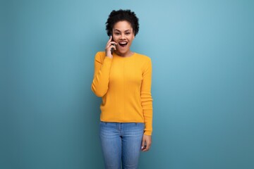 pretty 20s latin woman with afro hair in casual yellow blouse talking on the phone