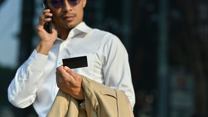 Worried millennial man holding credit card and talking on smartphone with customer service, having problem with credit card or payment