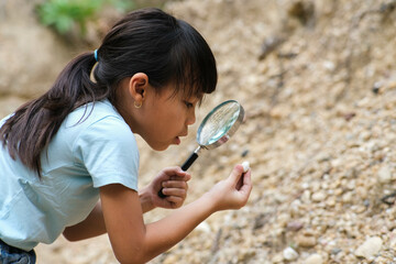 Cute little girl playing with stones and exploring with a magnifying glass. Little girl studying...