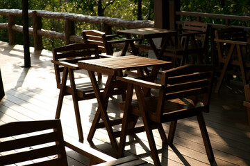Wooden tables and chairs at outdoor cafe terrace in park. Empty garden furniture surrounded by green garden.