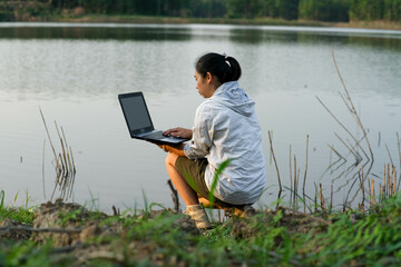 Female environmentalist using laptop computer to record natural water contamination checks. Biologist analyzing water test results using technology application on laptop. Water and ecology concept