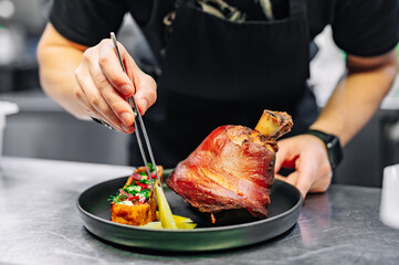 chef hand cooking Baked Pork knuckle with vegetables on plate in kitchen