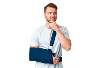 Young caucasian man with broken arm and wearing a sling over isolated chroma key background having doubts