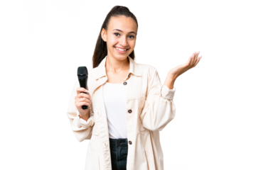 Young singer woman picking up a microphone over isolated chroma key background extending hands to the side for inviting to come
