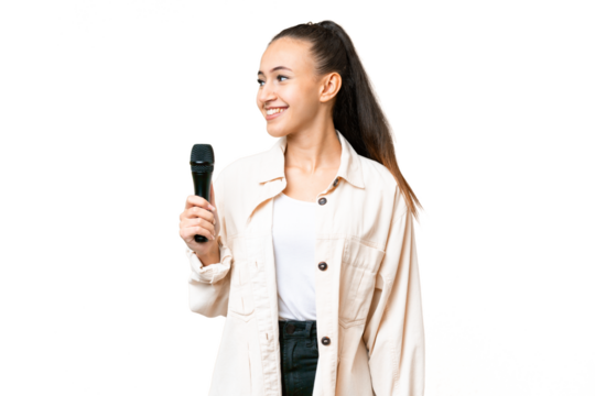 Young singer woman picking up a microphone over isolated chroma key background looking side