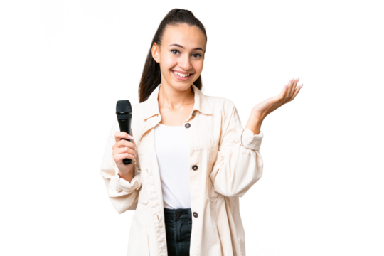 Young singer woman picking up a microphone over isolated chroma key background extending hands to the side for inviting to come