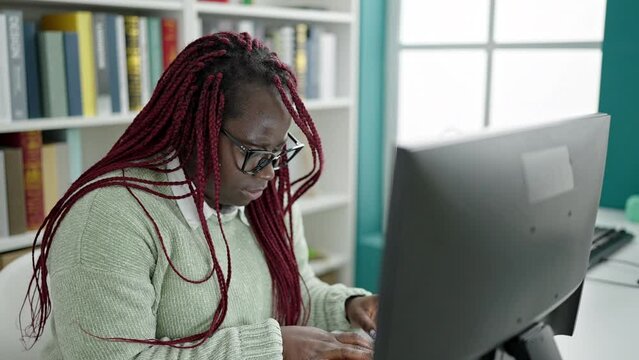 African woman with braided hair student using computer with neck ache at university library