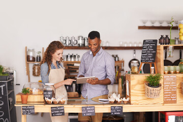 Fototapeta premium Restaurant owners, tablet and teamwork of people, manage orders and discussion in store. Waiters, black man and happy woman in cafe with technology for inventory, stock check and managing sales.