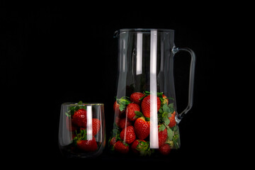 Strawberries in the beaker and glass dish with highlights on a black background. Fashionable presentation of the harvest.