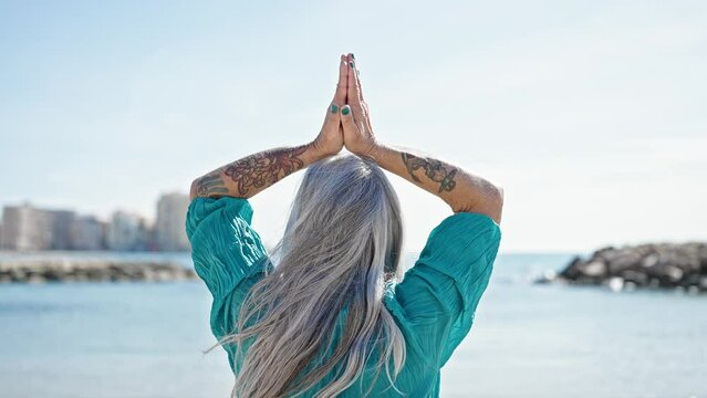 Middle age grey-haired woman doing yoga exercise at beach