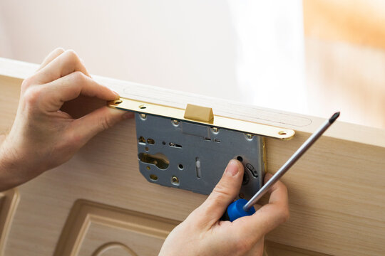 Handyman installing, repairing the door and lock. Closeup of worker hands installing new door lock.