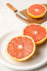 Fototapeta na wymiar Top view of cut red grapefruits on white plate and table with knife, selective focus, on white tablecloth, vertical, with copy space