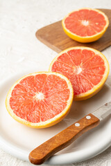 Fototapeta na wymiar Top view of cut red grapefruits on plate with knife and board, selective focus, on white tablecloth, vertical, with copy space