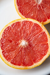Macro overhead view of cut red grapefruit on white plate, selective focus, vertical, with copy space
