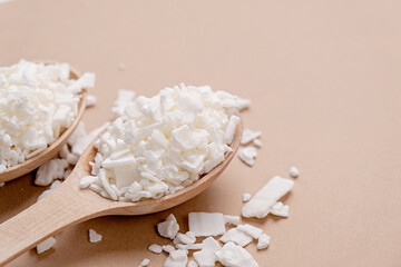 soy wax in wooden spoon on brown background, copy space