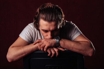 a young man sits leaning thoughtfully and upset on the back of a chair