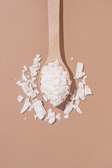 soy wax in wooden spoon on brown background, copy space