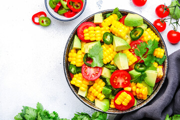 Mexican salad with sweet corn, avocado, jalapeno pepper, red tomatoes, cilantro and olive oil. White table background, top view