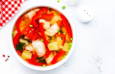 Fish soup with paprika, potatoes, tomatoes and parsley in ceramic soup bowl on white table background, top view