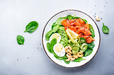 Ketogenic salad with salted salmon, avocado, spinach, cucumber, eggs and cashew nuts. Low-carbohydrate breakfast rich in healthy fats. Gray table background, top view