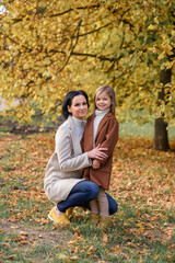 Fototapeta premium little beautiful girl with her mother hugging and kissing in the park in autumn in golden leaves