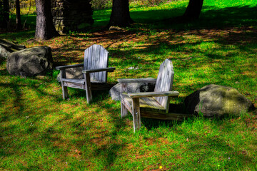 A pair of wooden Adirondack chairs in the grass next to the water's edge at Sky Lake in Windsor in Upstate NY. Two chairs inviting you to sit and relax and enjoy this Spring afternoon.
