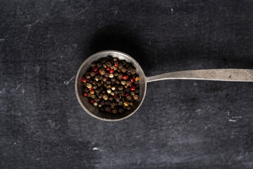 Big old spoon with peppercorn on black background