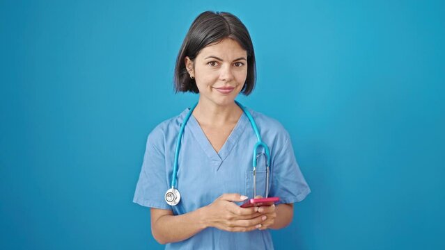 Young beautiful hispanic woman doctor smiling using smartphone over isolated blue background