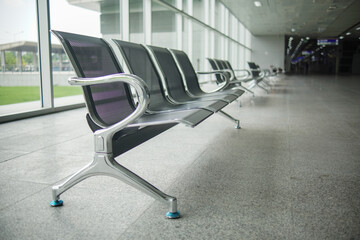 a row of metal benches sitting next to a window in an airport.