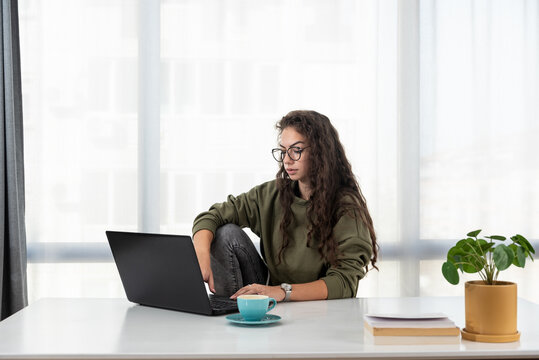 Stressed young woman holding head in hands and feeling demotivated while sitting at her home office and working remotely on laptop. Depressed female student tired of online learning and education