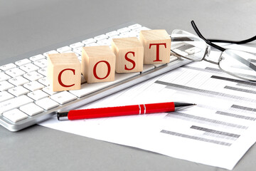 COST written on a wooden cube on the keyboard with chart on grey background