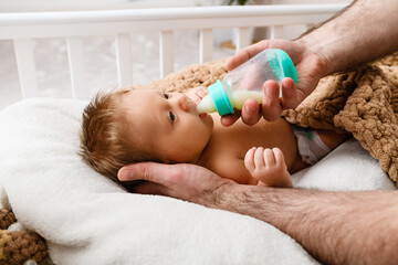Father hands feed infant with milk formula