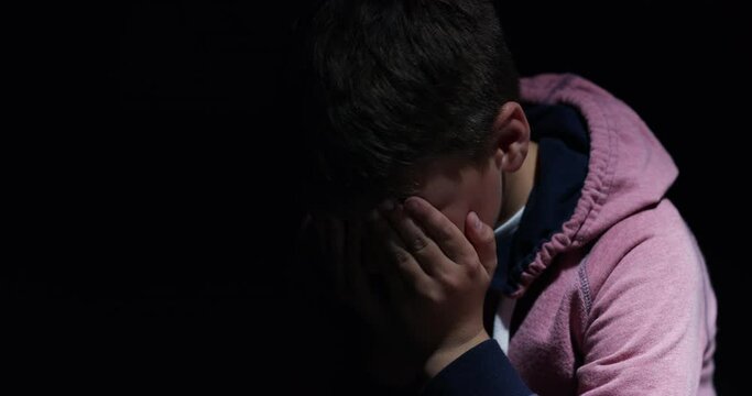 Child abuse, domestic violence and sad with a boy crying in a dark room feeling alone as a victim. Children, anxiety and fear with a young male kid looking scared or lonely and in need of help