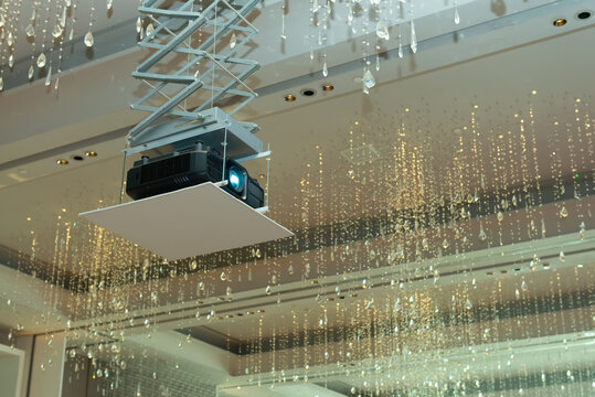 A photograph of a big projector hanging from the ceiling surrounded by crystal lamps in the function room. 