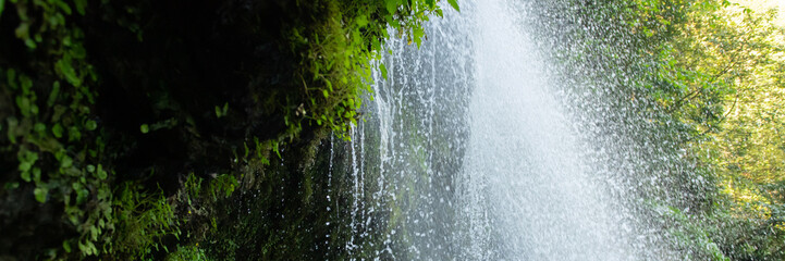 waterfall cascading down rocky cliffs by lush greenery banner