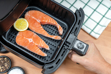 HAND COOKING RAW SALMON SLICES IN AIR FRYER BASKET IN THE KITCHEN. TOP VIEW.